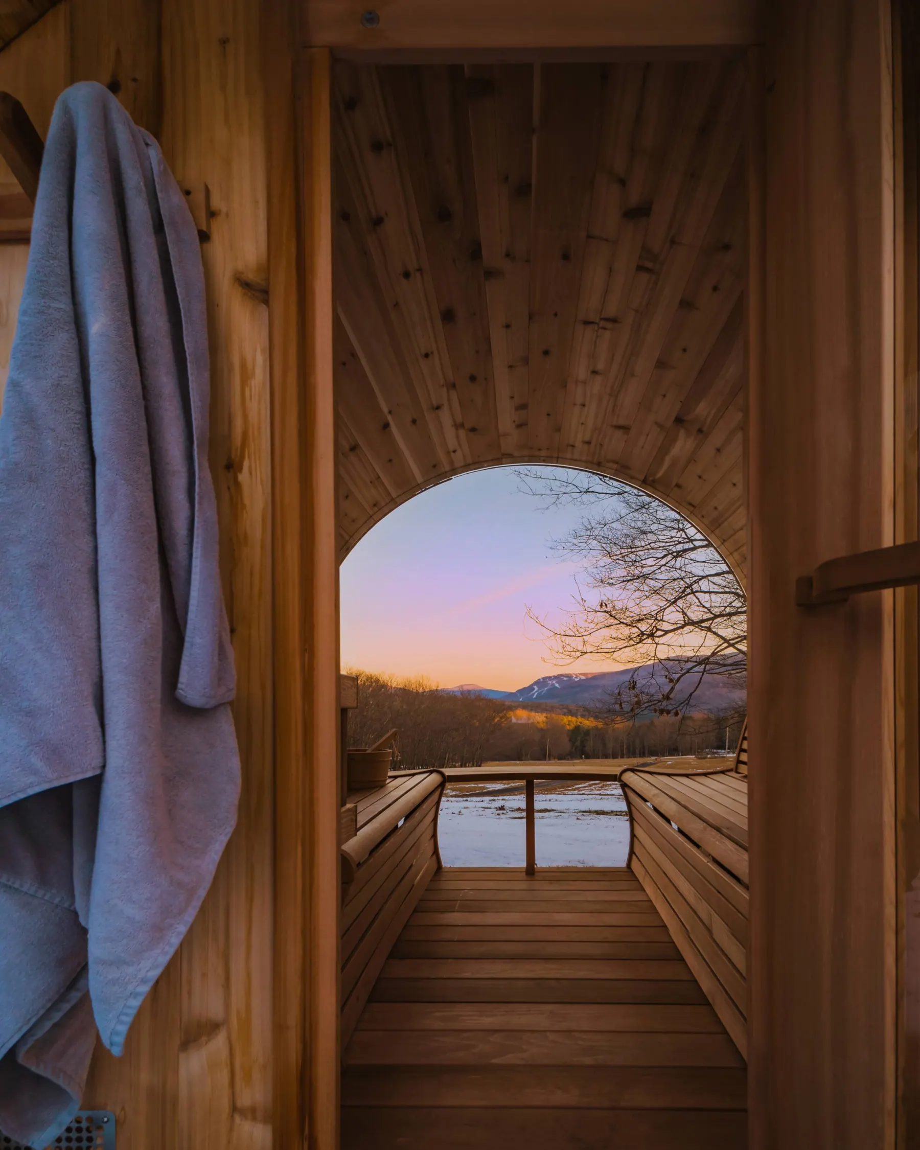 Inside the cedar barrel sauna, the panoramic window framing the valley at dusk